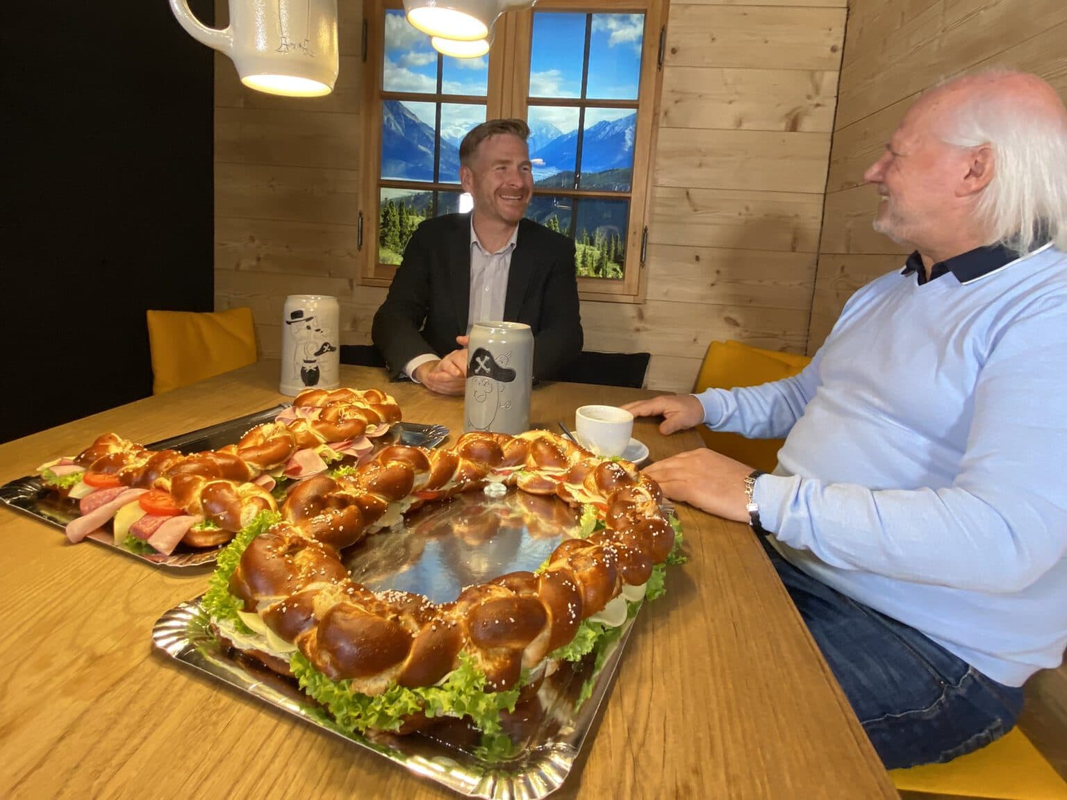 Interview zwischen Bernd Wandt, CEO von ServiceFactum und Mike Deiß, CEO von eggs unimedia. Beide schauen sich lachend an. Vor ihnen liegt eine Brezel in Form einer 10 als Sinnbild für die 10 erfolgreichen Jahre der gemeinsamen Partnerschaft.
