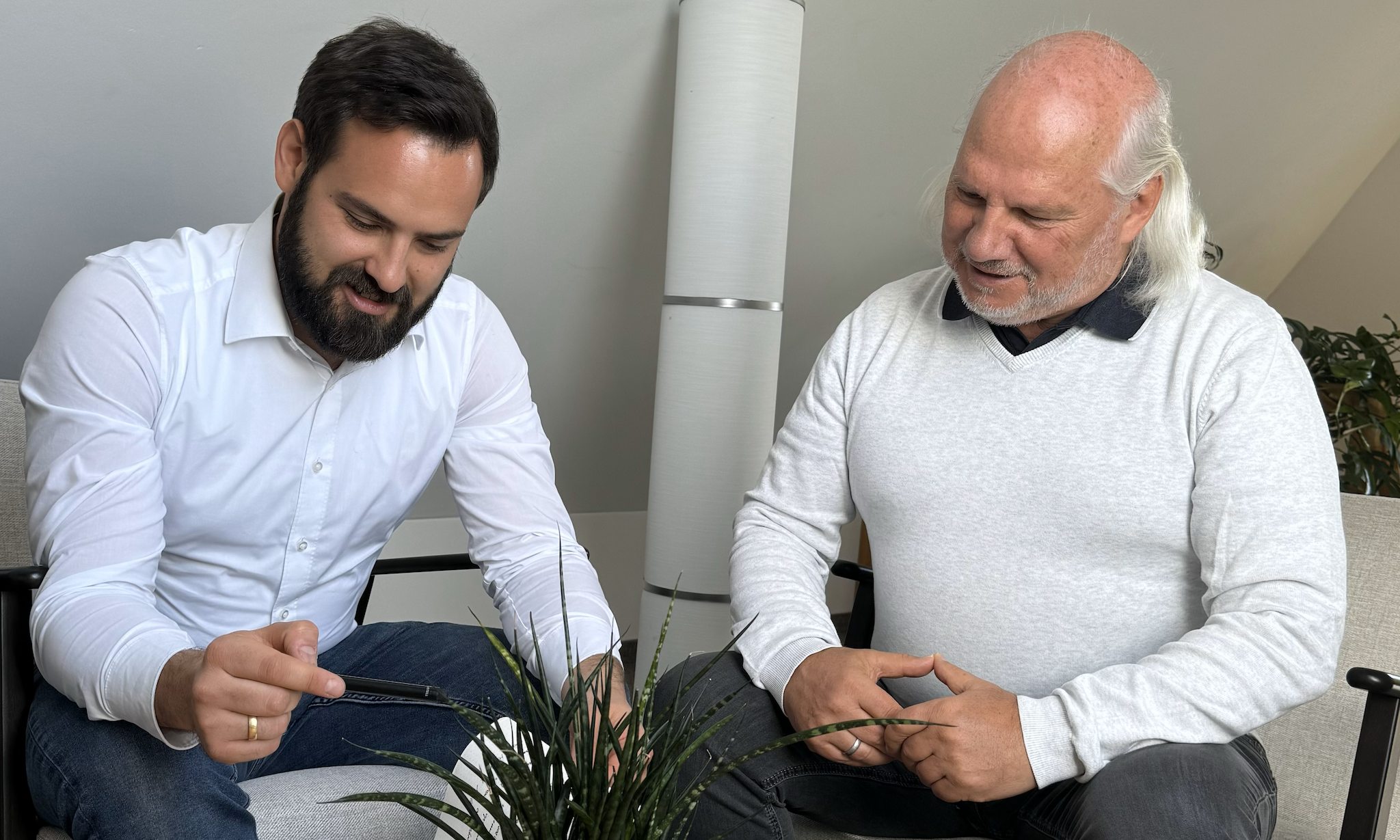 Bernd und Fabian schauen lächelnd auf ihr Notizblock und sind gerade in einer Besprechung für ServiceFactum. Sie sitzen beide im Loungebereich.
