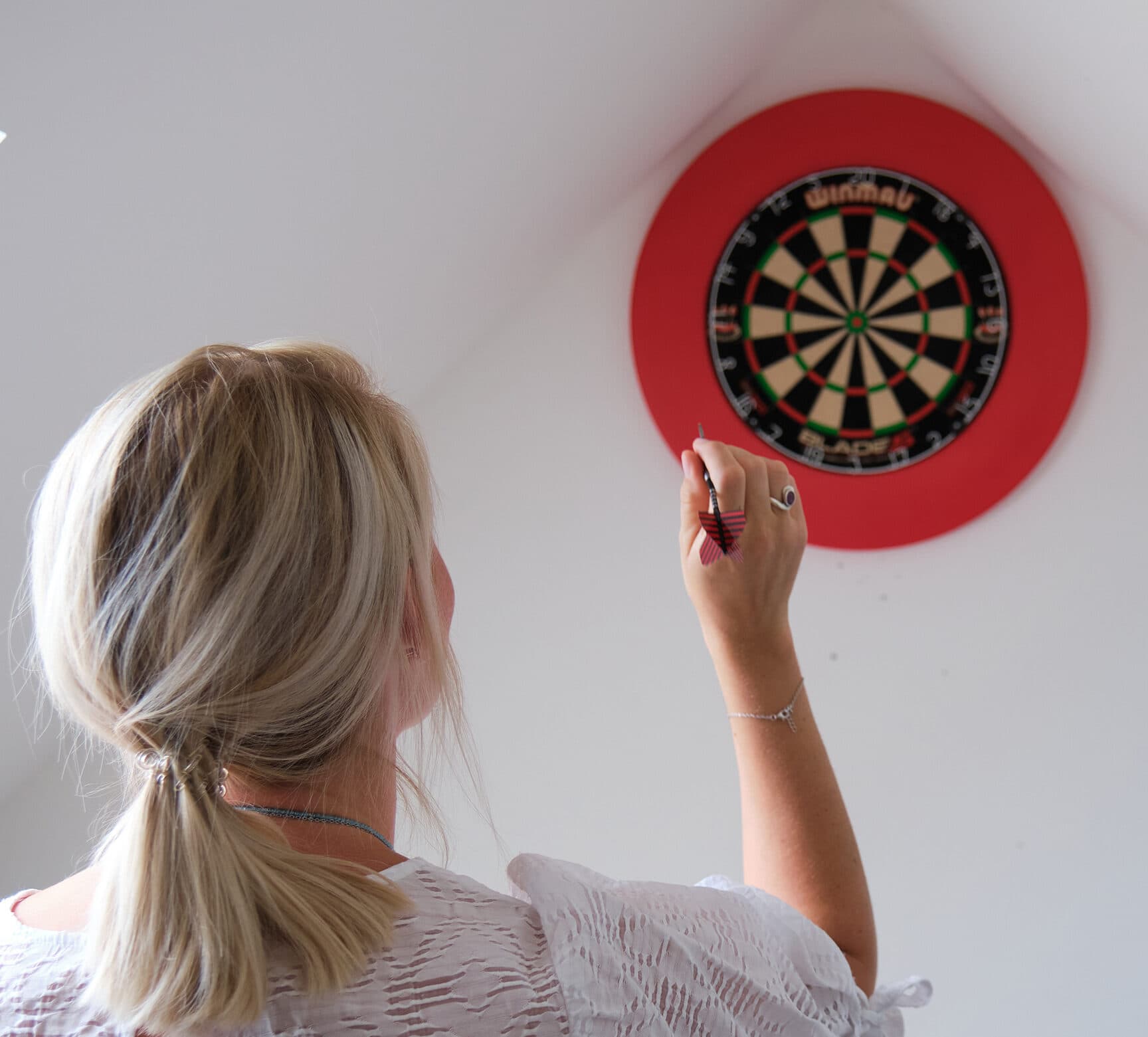 Eine Mitarbeitende von ServiceFactum sieht man von hinten, während sie einen Dartpfeil auf eine Dartscheibe wirft.