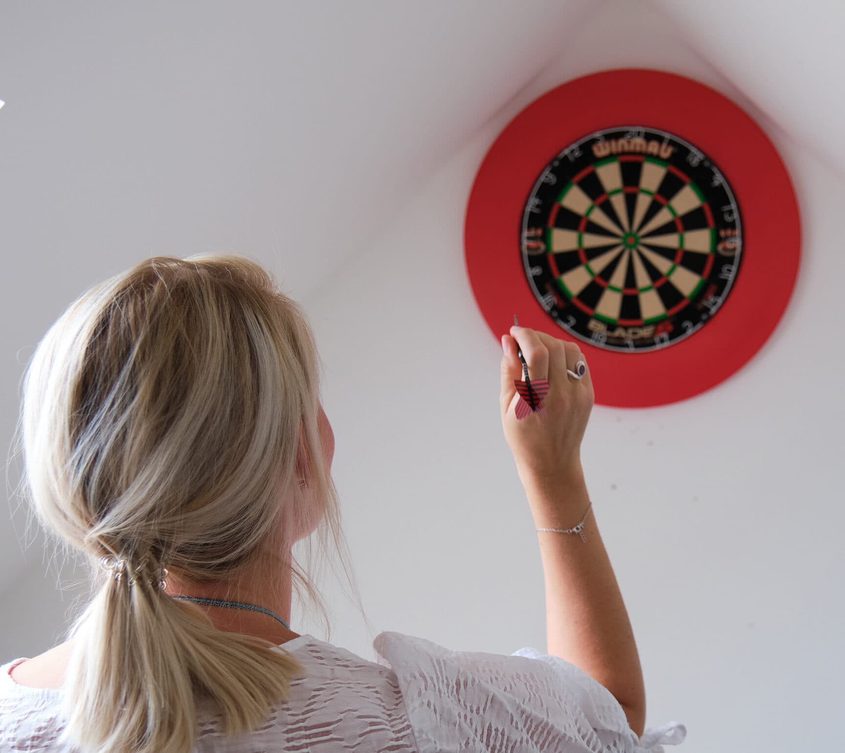 Eine Mitarbeitende von ServiceFactum sieht man von hinten, während sie einen Dartpfeil auf eine Dartscheibe wirft.