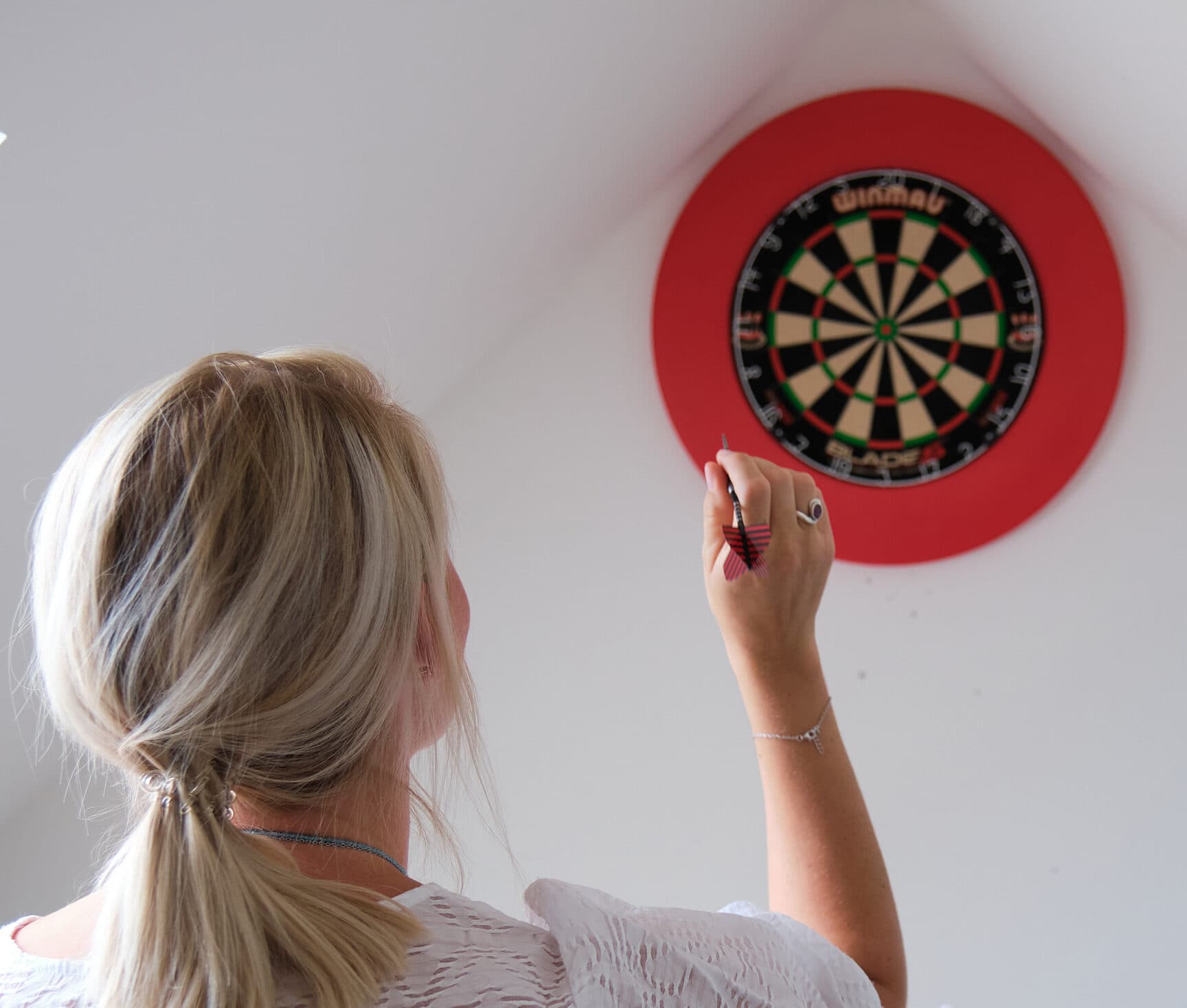 Eine Mitarbeitende von ServiceFactum sieht man von hinten, während sie einen Dartpfeil auf eine Dartscheibe wirft.