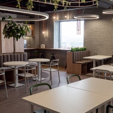 Bürolounge unseres Partners in Rumänien mit Sitzbänken, Pflanzen, Tischen und Stühlen.