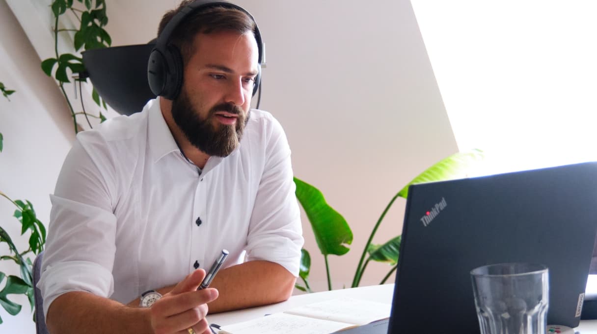 Unser Service Manager Fabian Ambrosi spricht mit einem unsere Kunden von ServiceFactum. Er hält einen Stift in der Hand und sitzt vor seinem Laptop mit Kopfhörer auf.