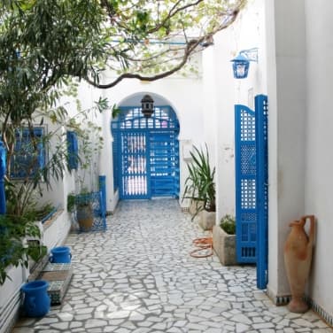 Charmantes Gebäude in einer tunesischen Kleinstadt mit blauen Türen, Lichtern und Vasen und einer weißen Fassade.
