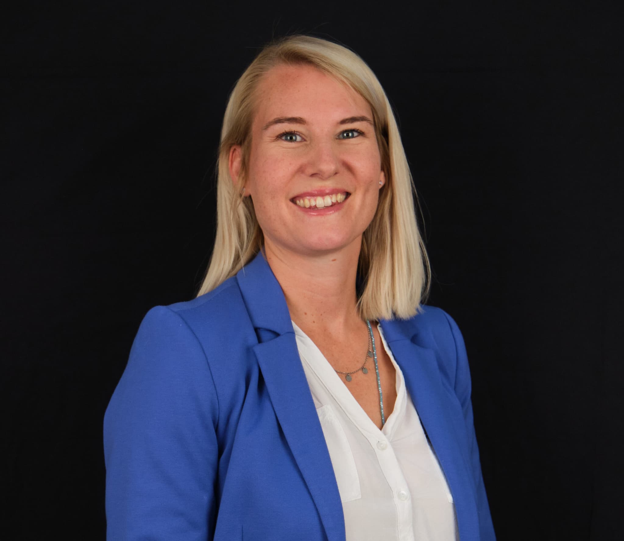 Ricarda Volk, Vertriebs- und Marketingexpertin bei ServiceFactum, schaut lächelnd in die Kamera. Sie steht vor einem schwarzen Hintergrund und hat ein blaues Sakko mit weißer Bluse an.