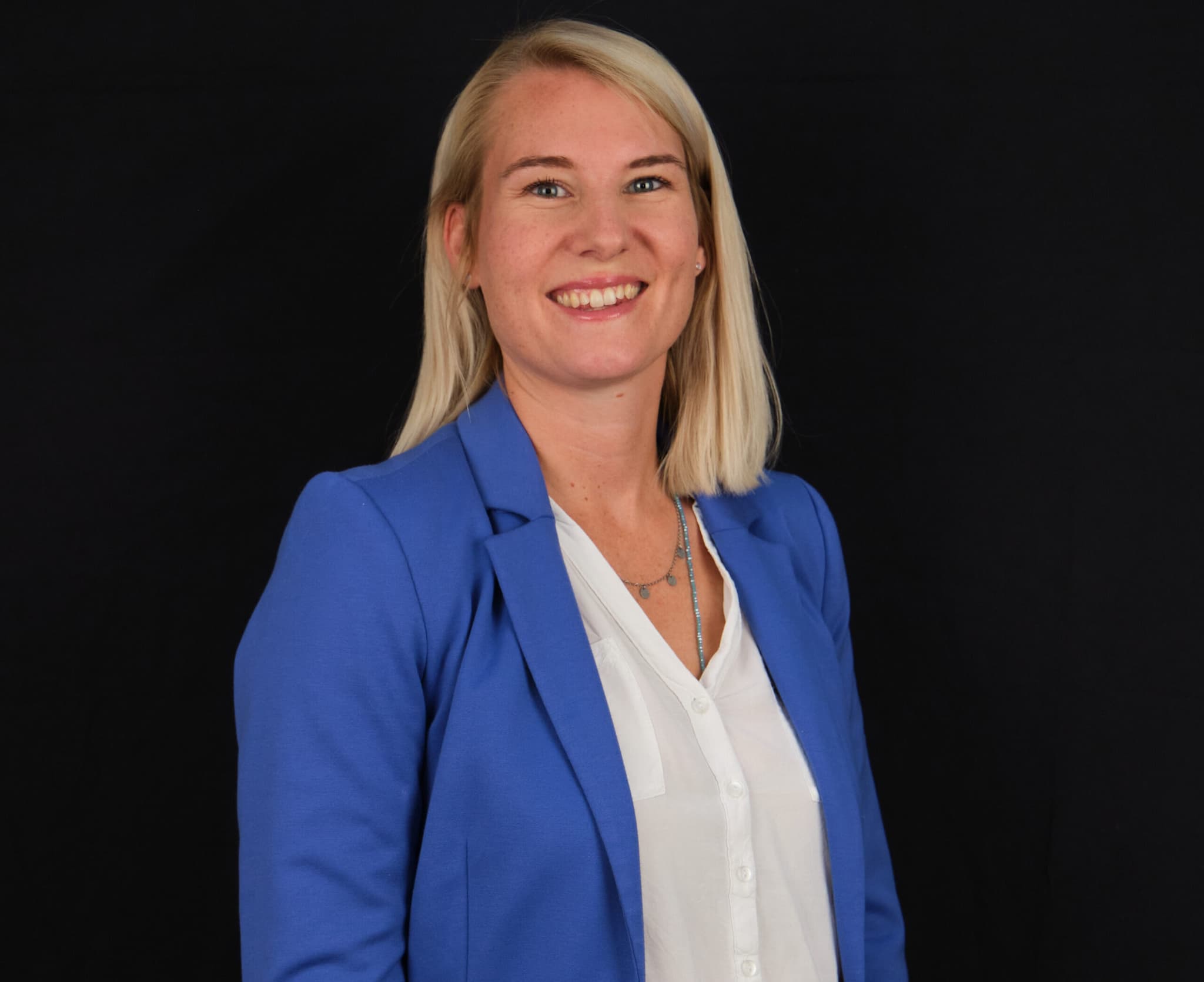 Ricarda Volk, Vertriebs- und Marketingexpertin bei ServiceFactum, schaut lächelnd in die Kamera. Sie steht vor einem schwarzen Hintergrund und hat ein blaues Sakko mit weißer Bluse an.